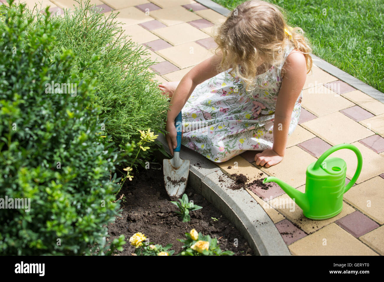 Little blonde girl planting flower in a garden Stock Photo - Alamy