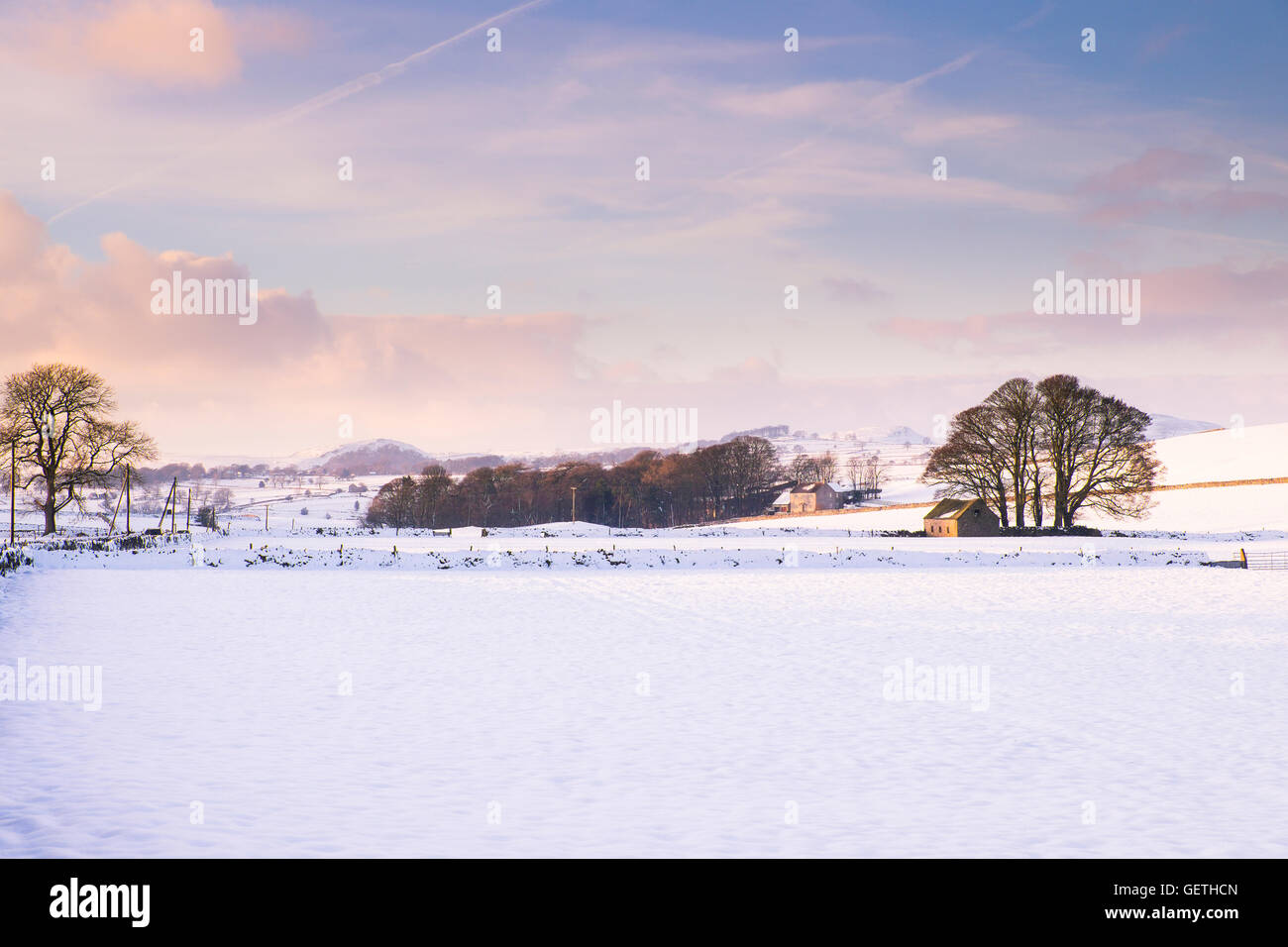View across snowy farmland near Ashbourne at sunset on a winter evening. Stock Photo