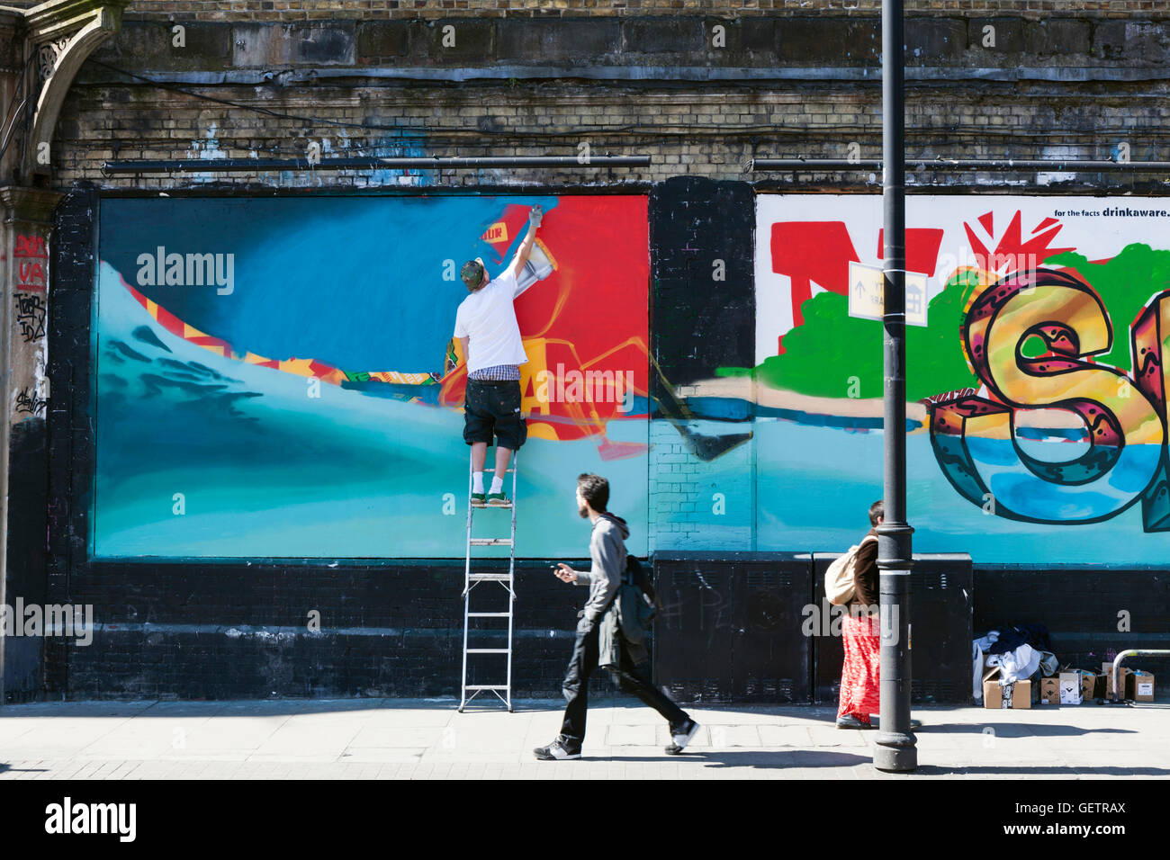 A street artist spray paints a mural on a wall in Shoreditch Stock ...