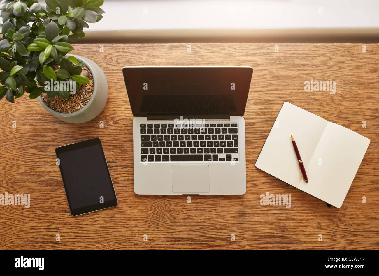 Top view shot of laptop computer, digital tablet, potted plant, diary and pen on wooden worktable. Stock Photo