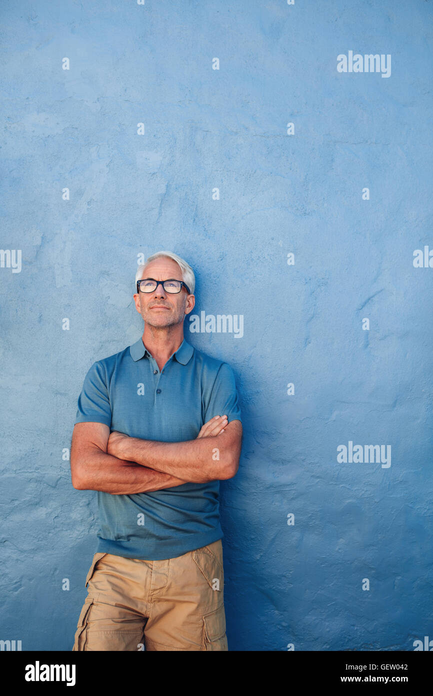 Portrait of confident mature man standing against a blue background. Handsome  male in glasses standing with his arms crossed an Stock Photo