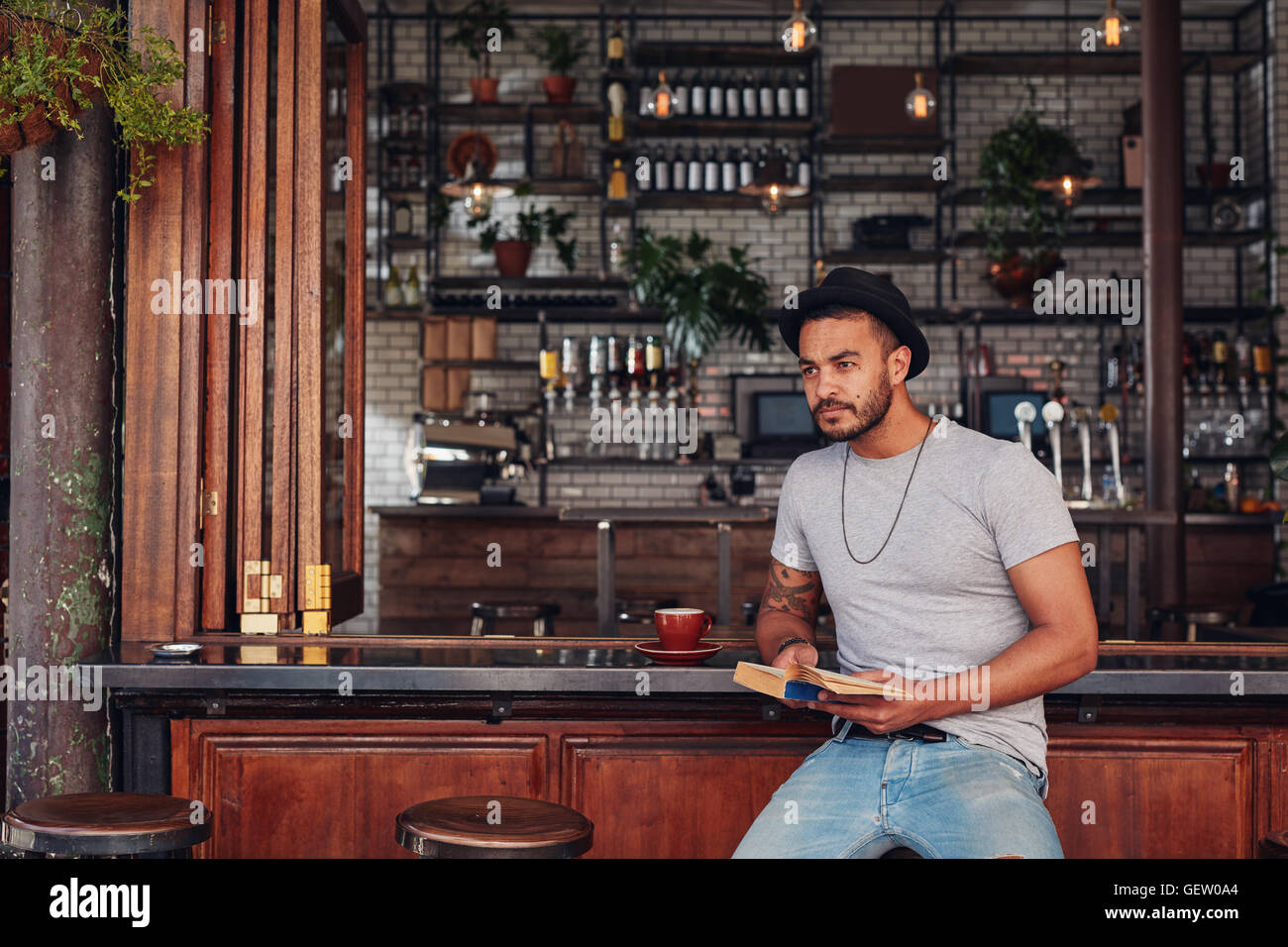 Portrait of trendy young male sitting at a cafe counter with a book. Stylish young male with novel at a coffee shop. Stock Photo