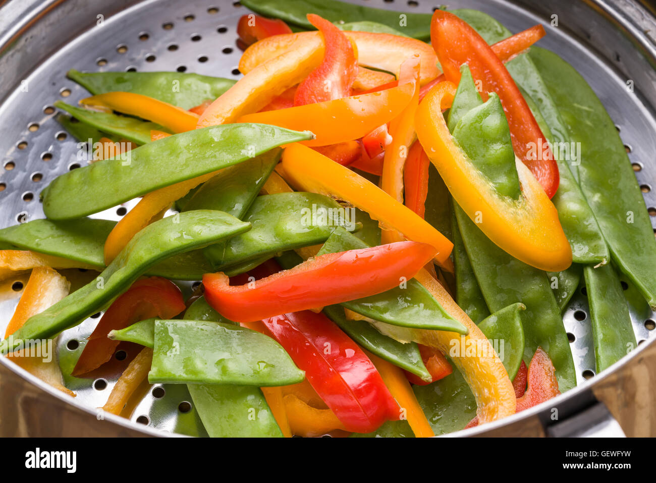 Bell pepper and snow pea stir-fry in stainless steel colander Stock Photo