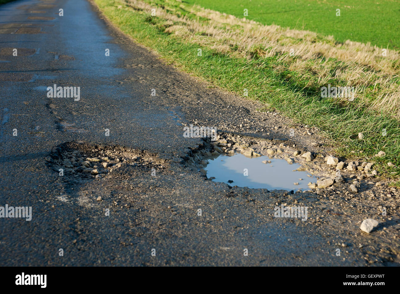 Pothole in the road filled with water. Stock Photo