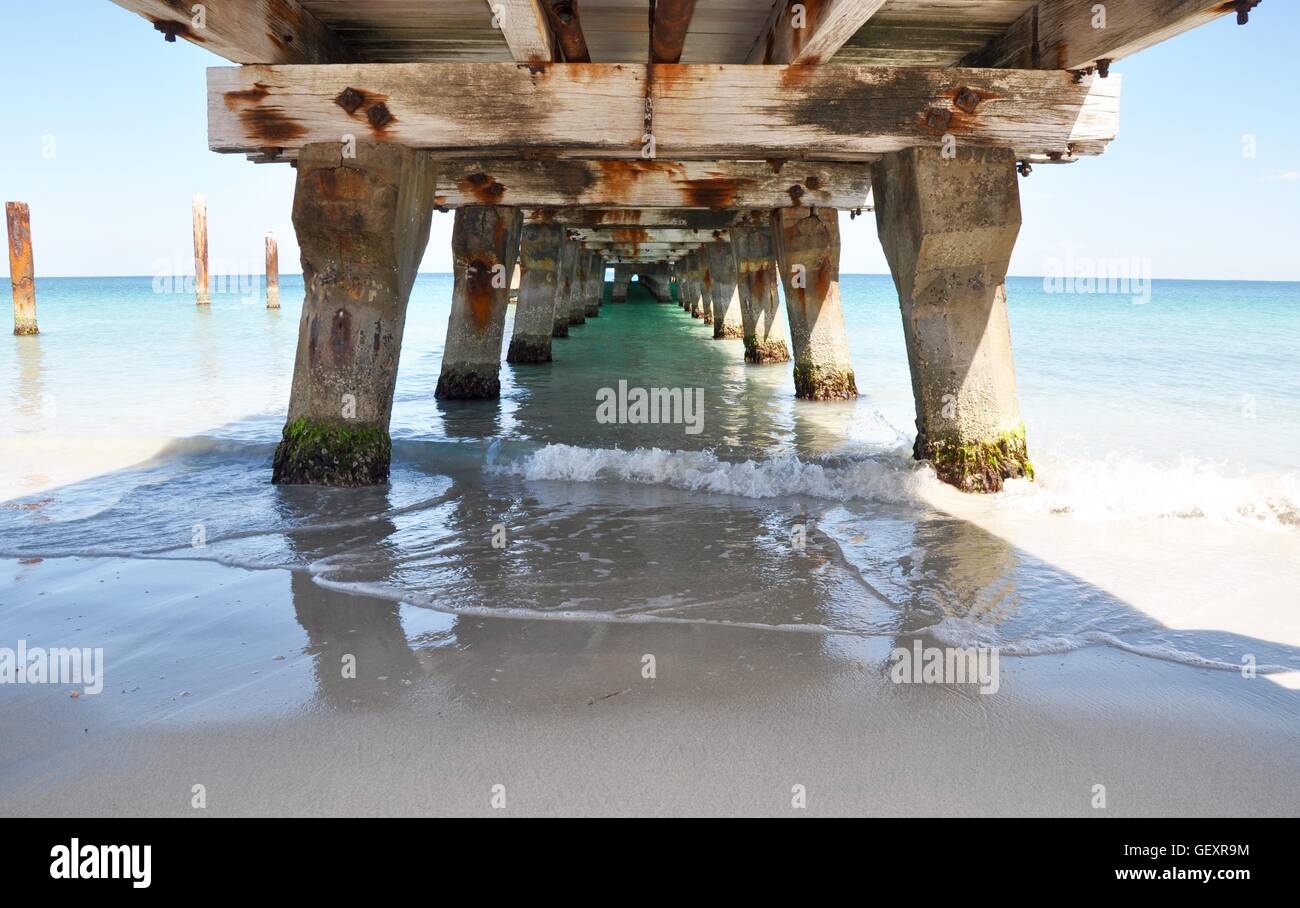 View underneath the Coogee Beach jetty in diminishing perspective with Indian Ocean waves under a blue sky in Western Australia. Stock Photo