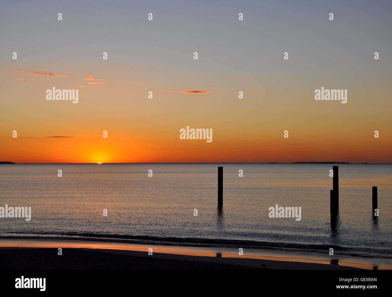 Orange glowing Indian Ocean sunset with calm waters and pilings at Coogee Beach in Coogee, Western Australia. Stock Photo