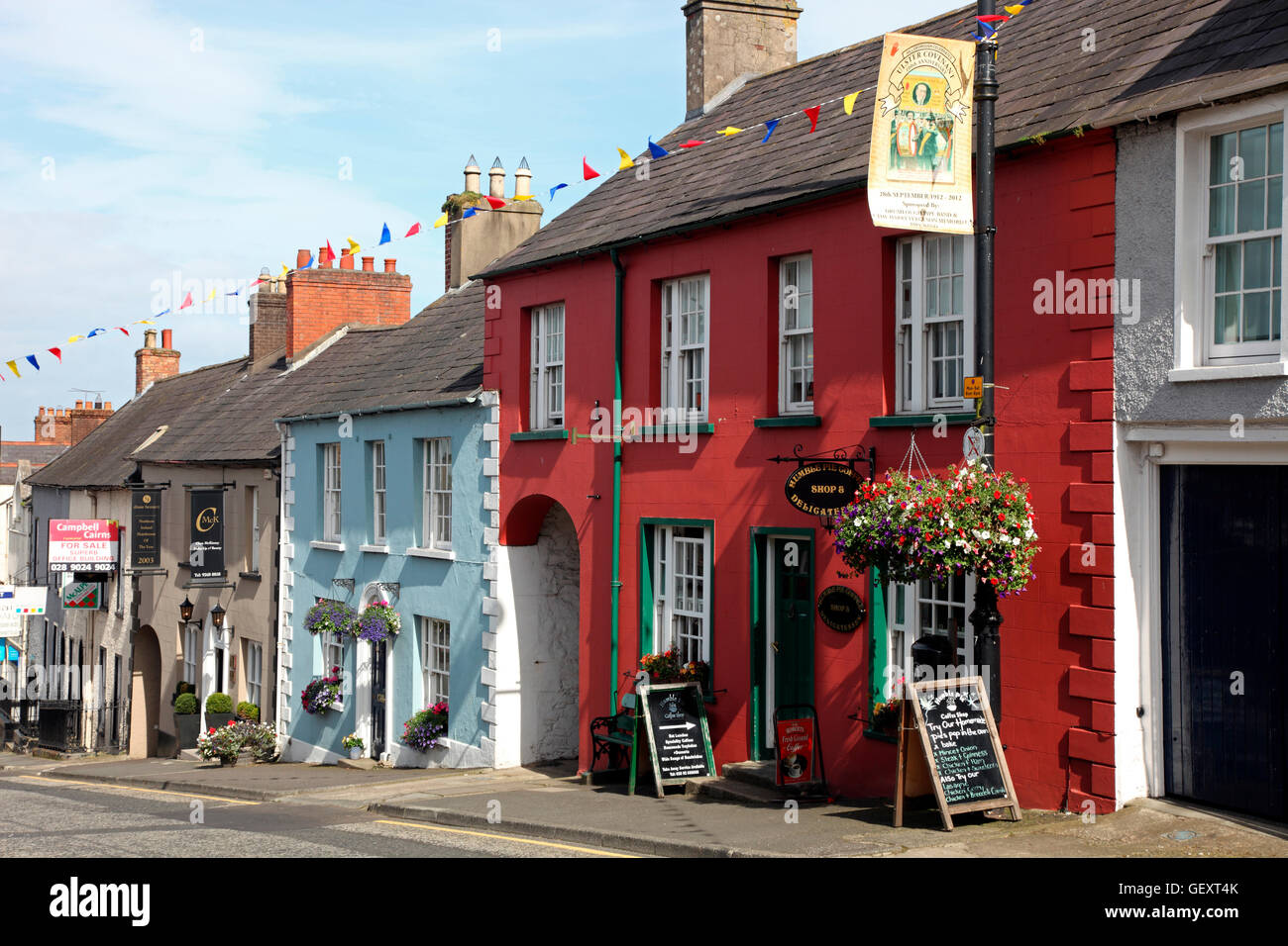 Charming Main Street in Hillsborough village, Northern Ireland, lined with traditional historic buildings, small shops, and vibrant floral baskets, with people strolling.