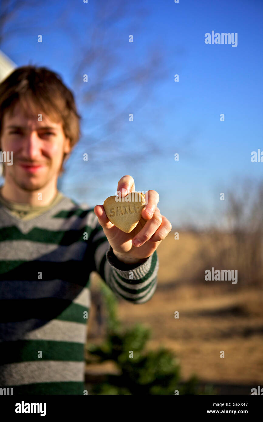 Man holding heart shaped cookie with the word smile written on it. Stock Photo