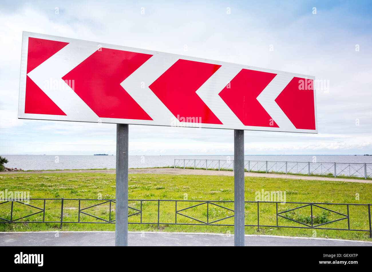 Dangerous turn. Red and white stripped arrow. Road sign in summer city Stock Photo