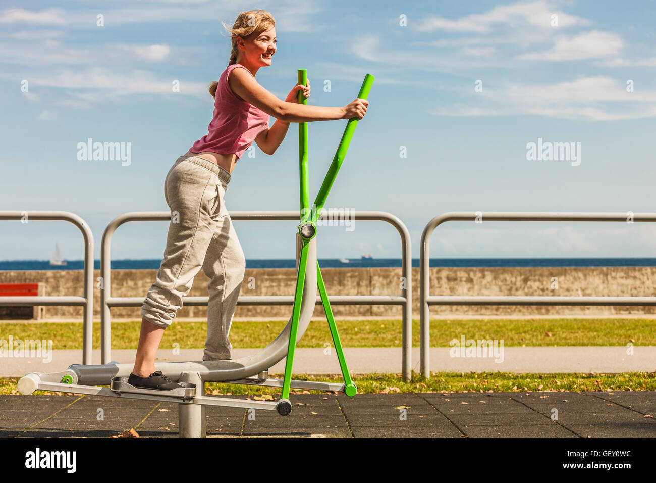 Active young woman exercising on elliptical trainer machine. Fit sporty girl in training suit working out at outdoor gym. Sport Stock Photo