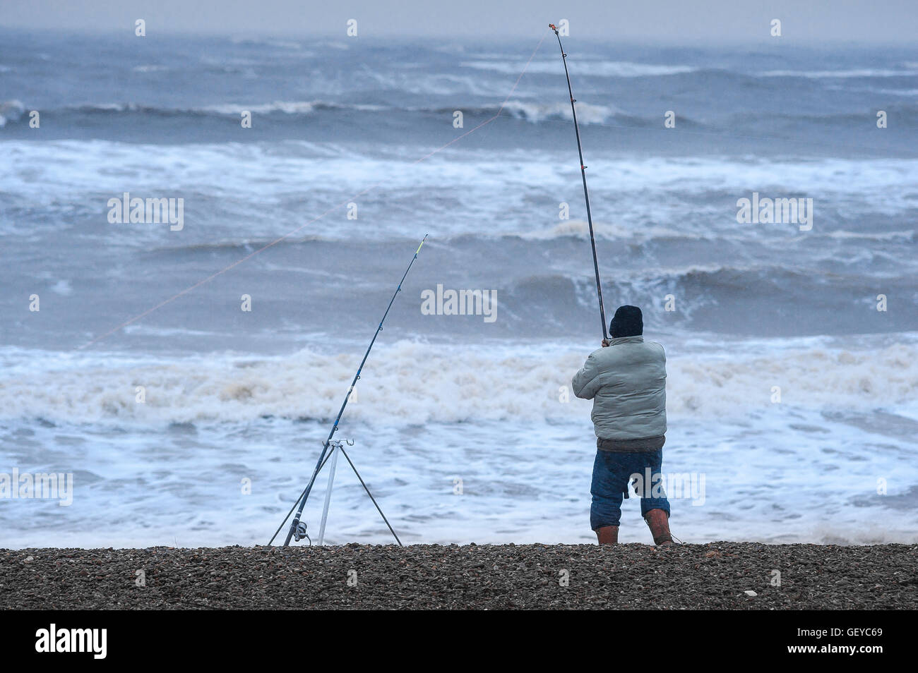 Man fishing stormy weather, rear view of a man fishing from the beach during rough weather at Dunwich on the Suffolk coast, England. Stock Photo