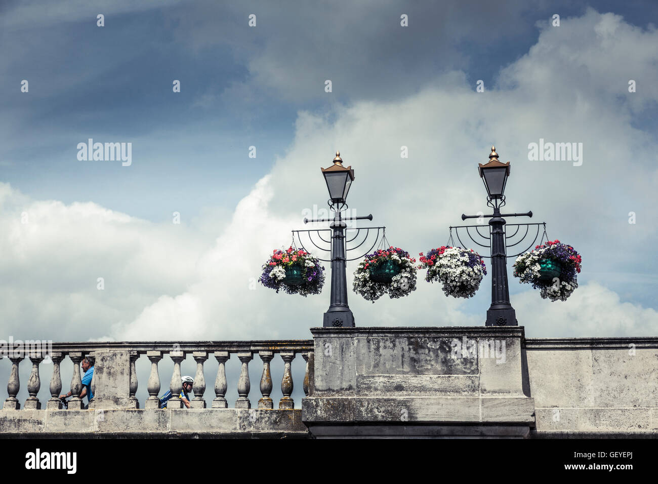 Two cyclists pass each other beneath colourful hanging baskets on the