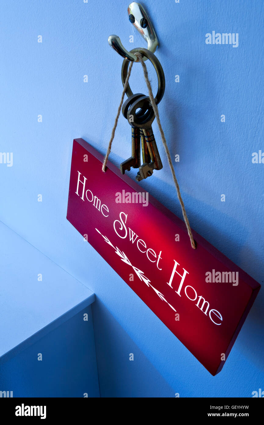 HOME BUYING FIRST TIME BUYERS PURCHASE CONCEPT Moody atmospheric 'Home Sweet Home' sign hanging with door keys on hook with shaft of sunlight Stock Photo