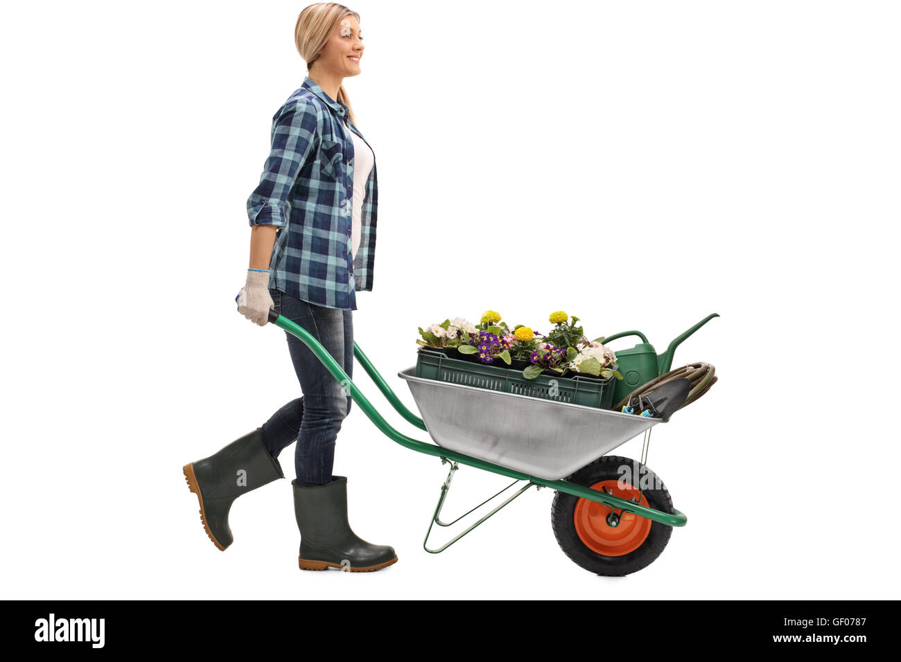 Cheerful blond woman pushing a wheelbarrow with gardening equipment isolated on white background Stock Photo