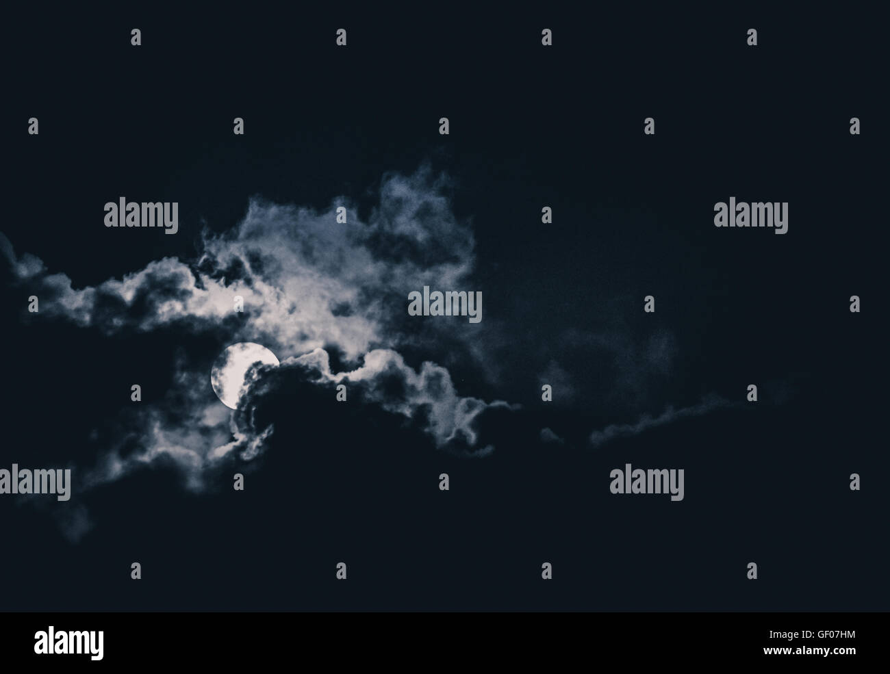 Full Moon Behind Clouds Glowing On A Dark Night Sky Stock Photo