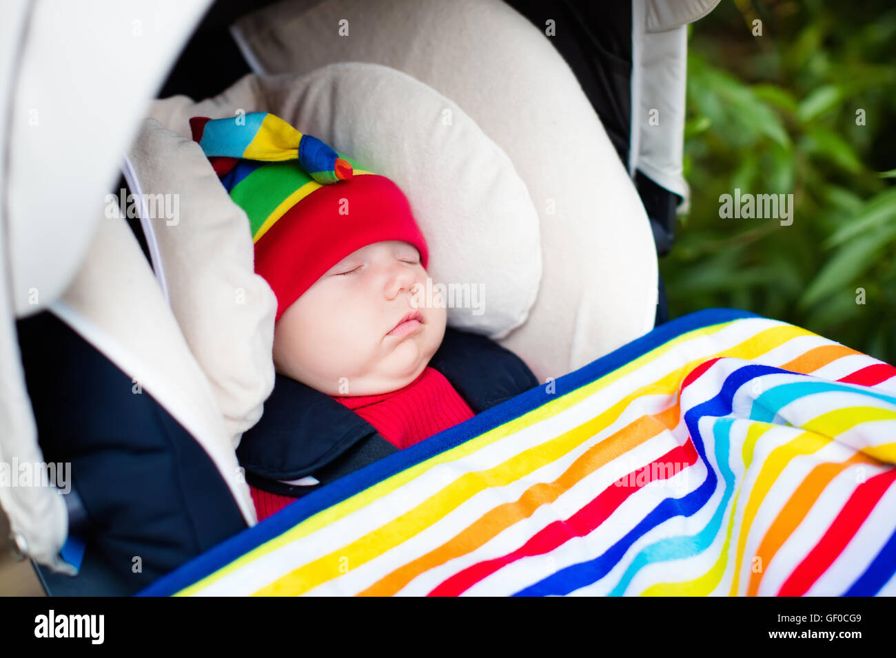 Cute little baby in funny colorful hat sleeping in infant car seat on a walk in a park Stock Photo