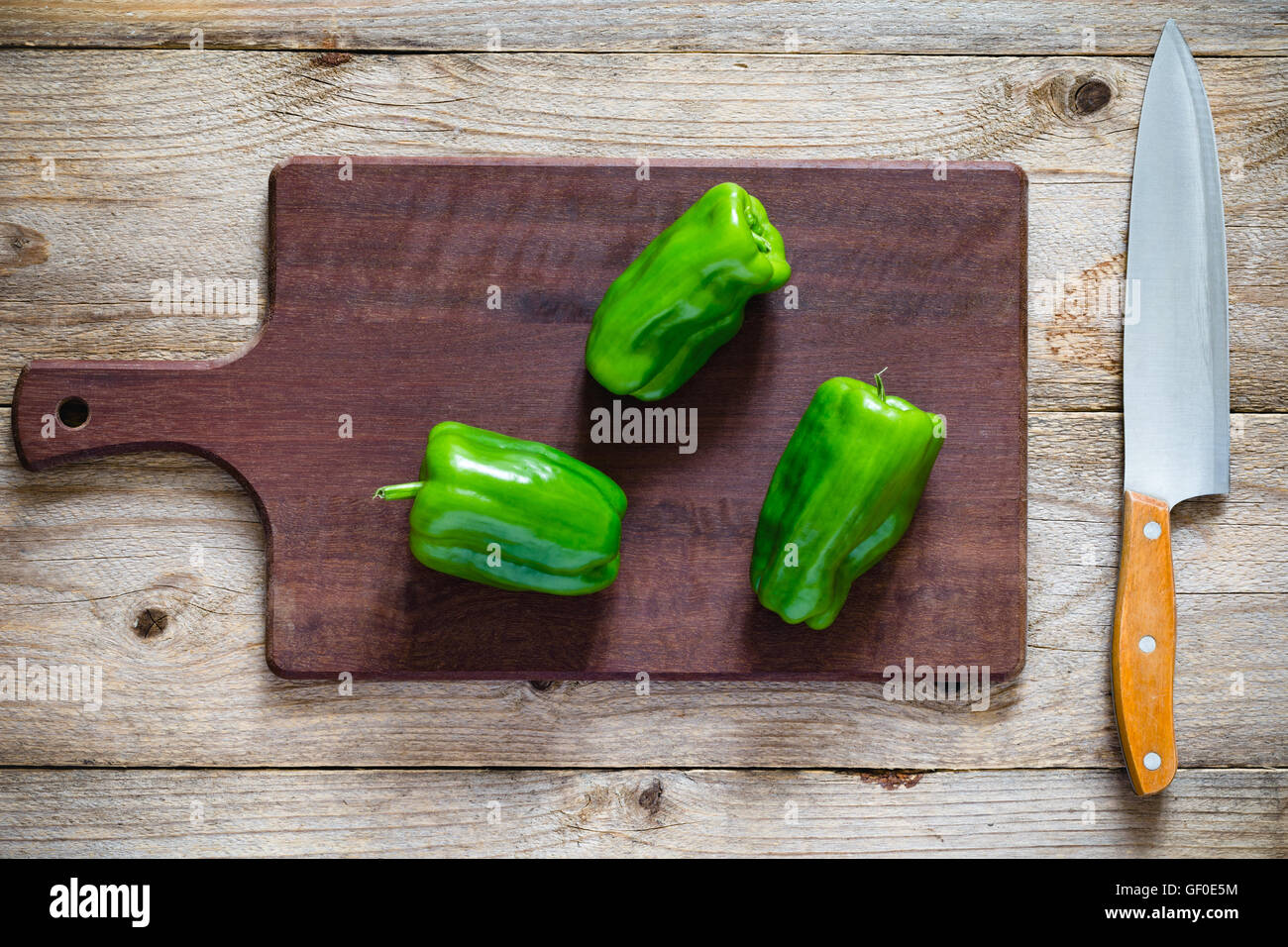 Green bell peppers on wooden chopping board and a knife. Overhead view ...