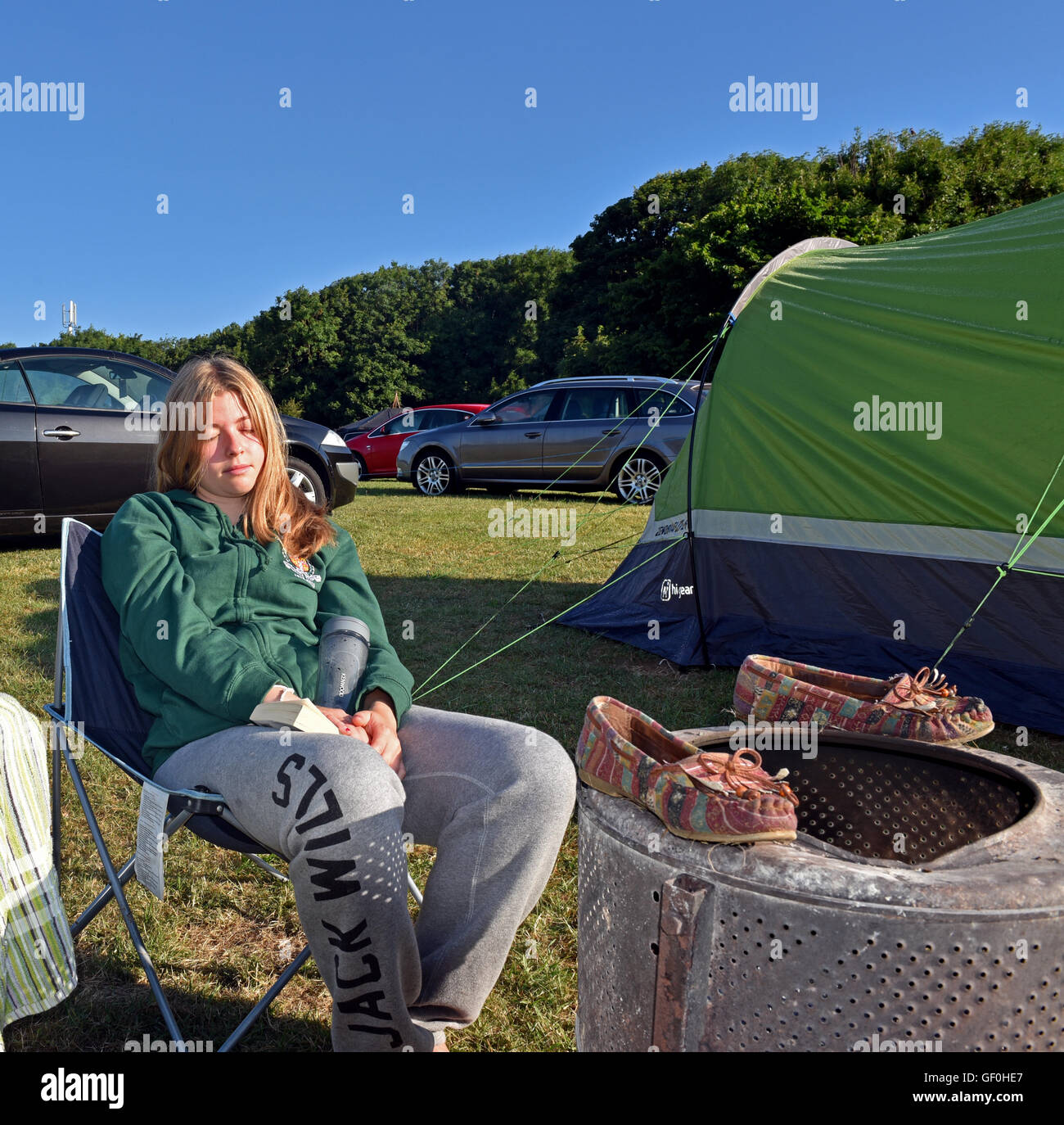 girl sits drying her shoes by the camp fire Stock Photo