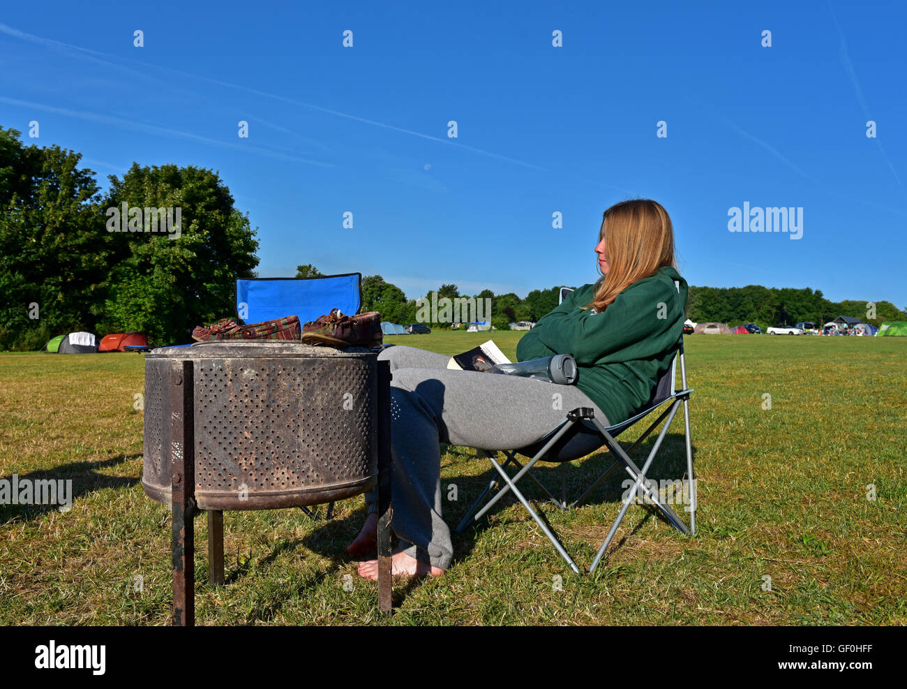 girl sits drying her shoes by the camp fire Stock Photo