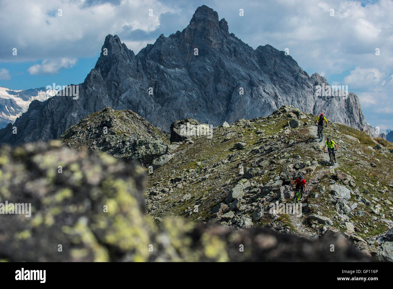 Three mountain bikers ride the ridge between Courchevel and Meribel away from the Aiguille du Fruit peak in the French Alps Stock Photo
