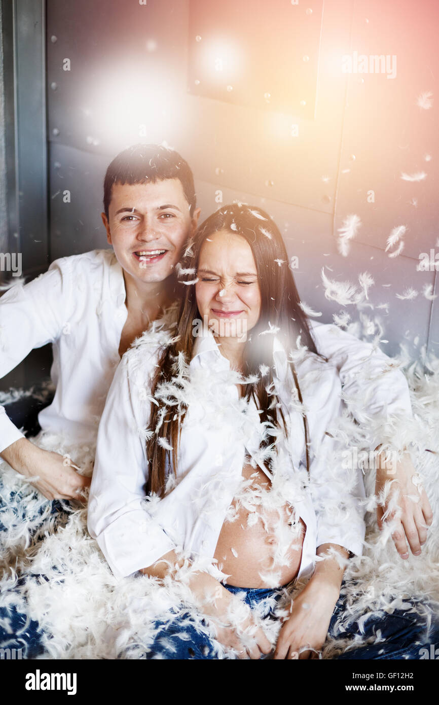 Pillow fight. Young happy couple have fun. Man and woman dressed in jeans and white shirts. Stock Photo