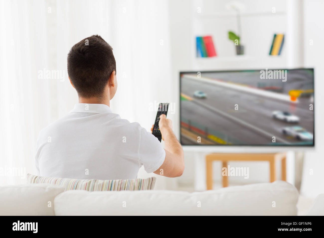 man with remote watching motorsports on tv at home Stock Photo
