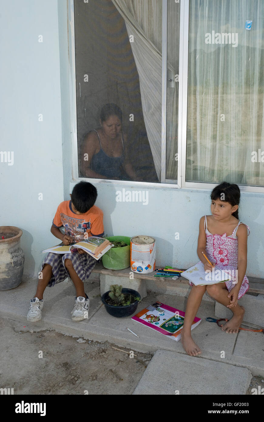 Young boy and girl do their homework outside the window of their house in Escobedo, Nuevo León state, Mexico. Stock Photo