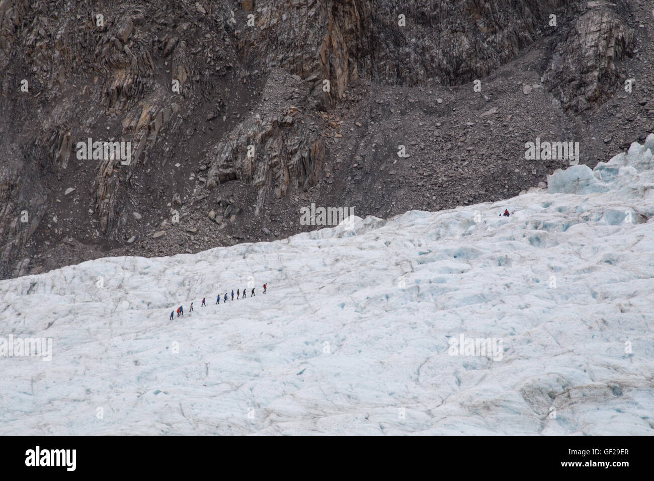 Franz Josef, New Zealand - March 22, 2015: A group of tourists hiking in the distance on Franz Josef Glacier. Stock Photo
