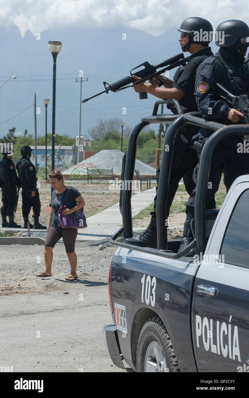 A woman walks on a street in the Colonia Alianza Real in Escobedo, Nuevo Leon under the watchful eye of armed police. Stock Photo