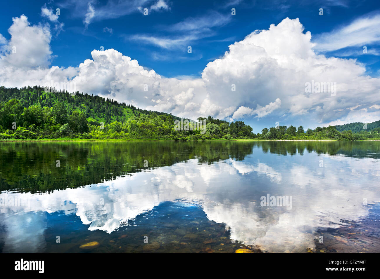 Beautiful landscape with cloudy blue sky reflected in the clear river water. Wooded waterside of a mountain lake. Summer idyllic Stock Photo