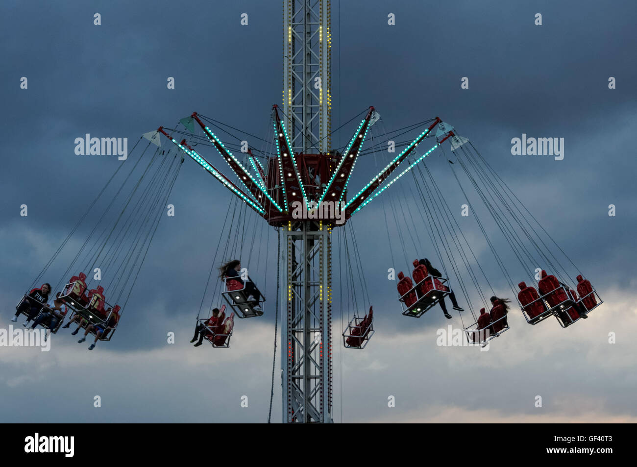 People enjoying swing ride with dark clouds in the background Stock Photo