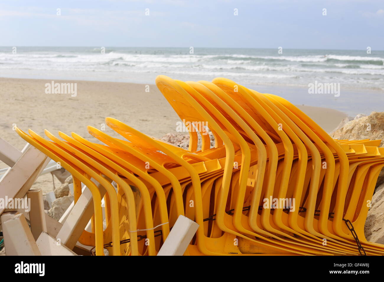 Stack of Yellow Chairs.  Yellow plastic chairs stacked and tied with a chain on the beach out of bathing season, along with other coffee shop furnitur Stock Photo