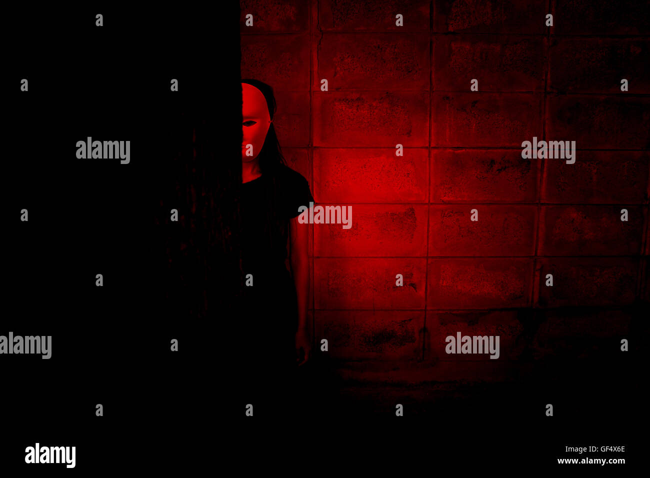 Mysterious woman in black dress wearing white mask hiding behind tree,Scary background for halloween Stock Photo