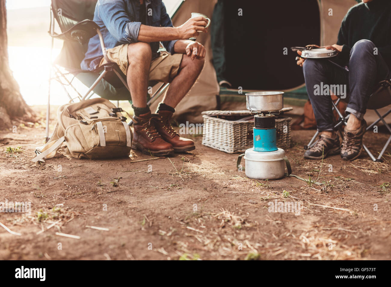 Cropped image of a couple sitting outside the tent and making coffee on a camp stove. Stock Photo