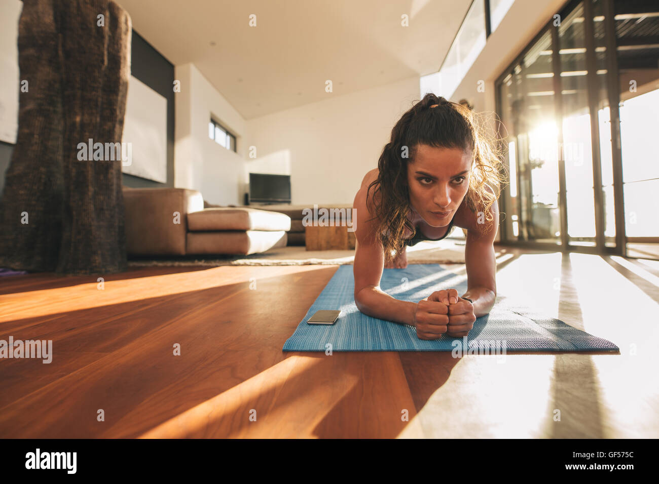 Shot of fit young woman doing plank at home. Healthy young female working out on exercise mat. Stock Photo