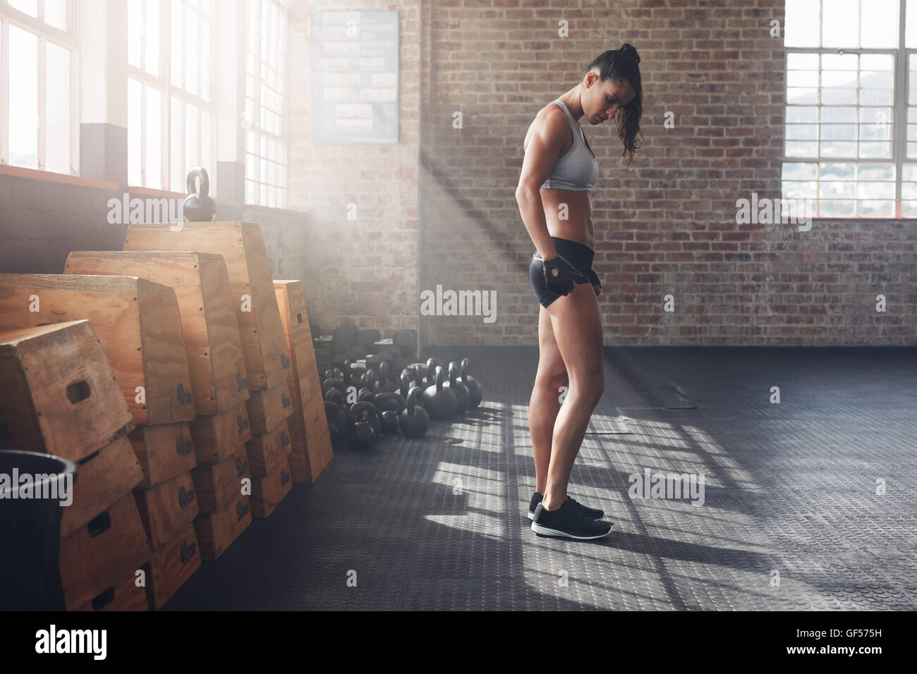 Full length indoor shot of determined young woman standing in gym. Tough female athlete at crossfit gym with exercise equipments Stock Photo