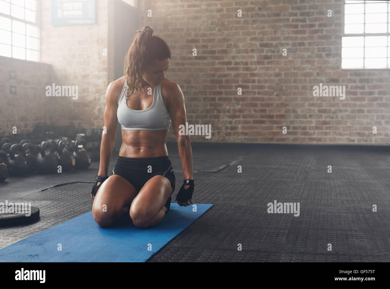 Shot of fitness woman sitting on exercise mat and looking at her triceps. Muscular woman working out at the fitness club. Stock Photo