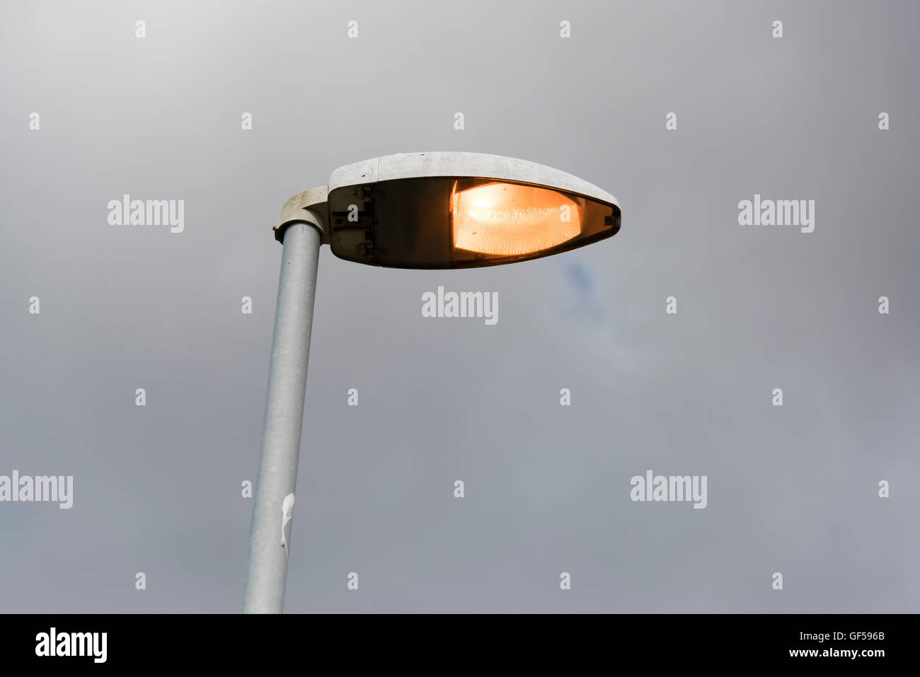 A street lamp close up, turned on in the daytime against a grey sky Stock Photo