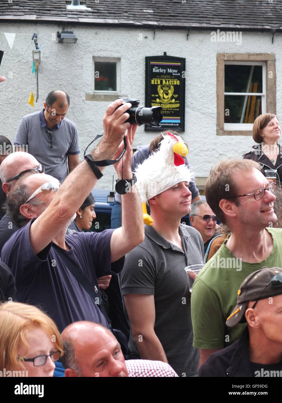 Spectators, including a man in a chicken hat, watch chickens race at the annual Bonsall World Championship Hen Racing Stock Photo