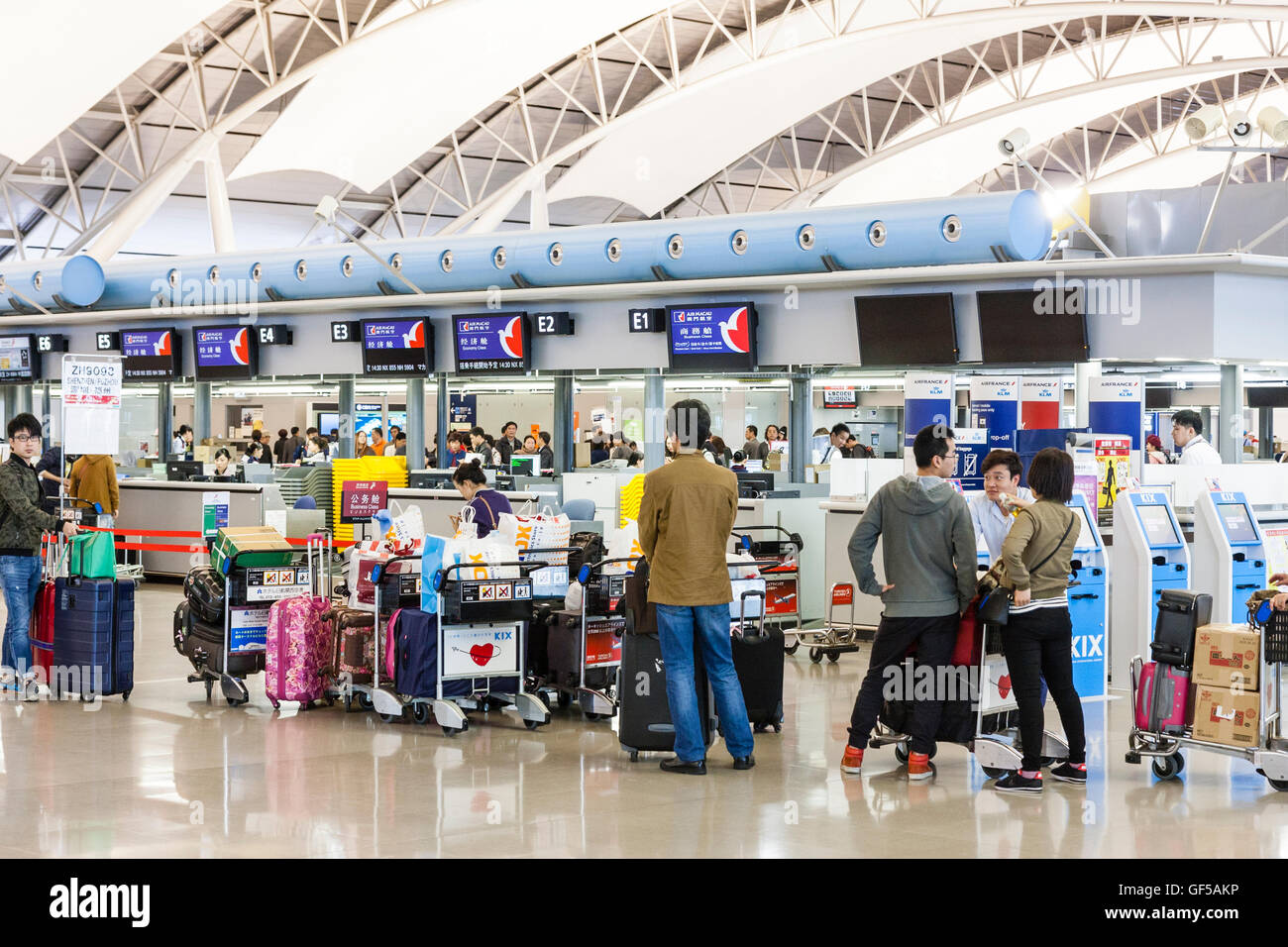 Japan, Kansai airport, KIX. Interior, terminal one. International check-in. Queues of Asian people with baggage trollies, waiting to check in at desks. Stock Photo