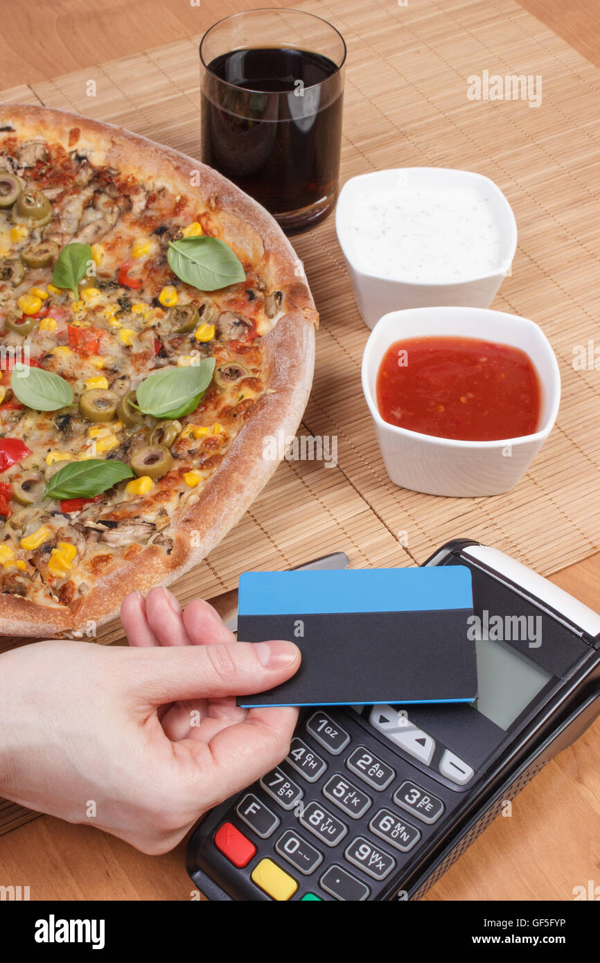 Using payment terminal with contactless credit card, cashless paying for vegetarian pizza in restaurant, Stock Photo