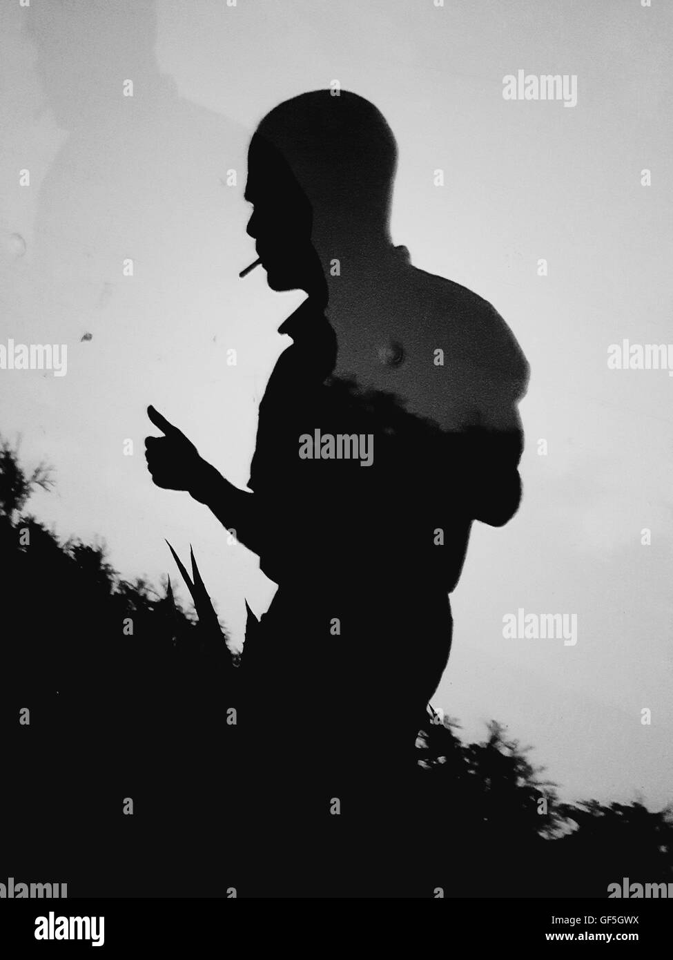 Multiple shadows on wall of man with cigarette showing a thumb up sign ...