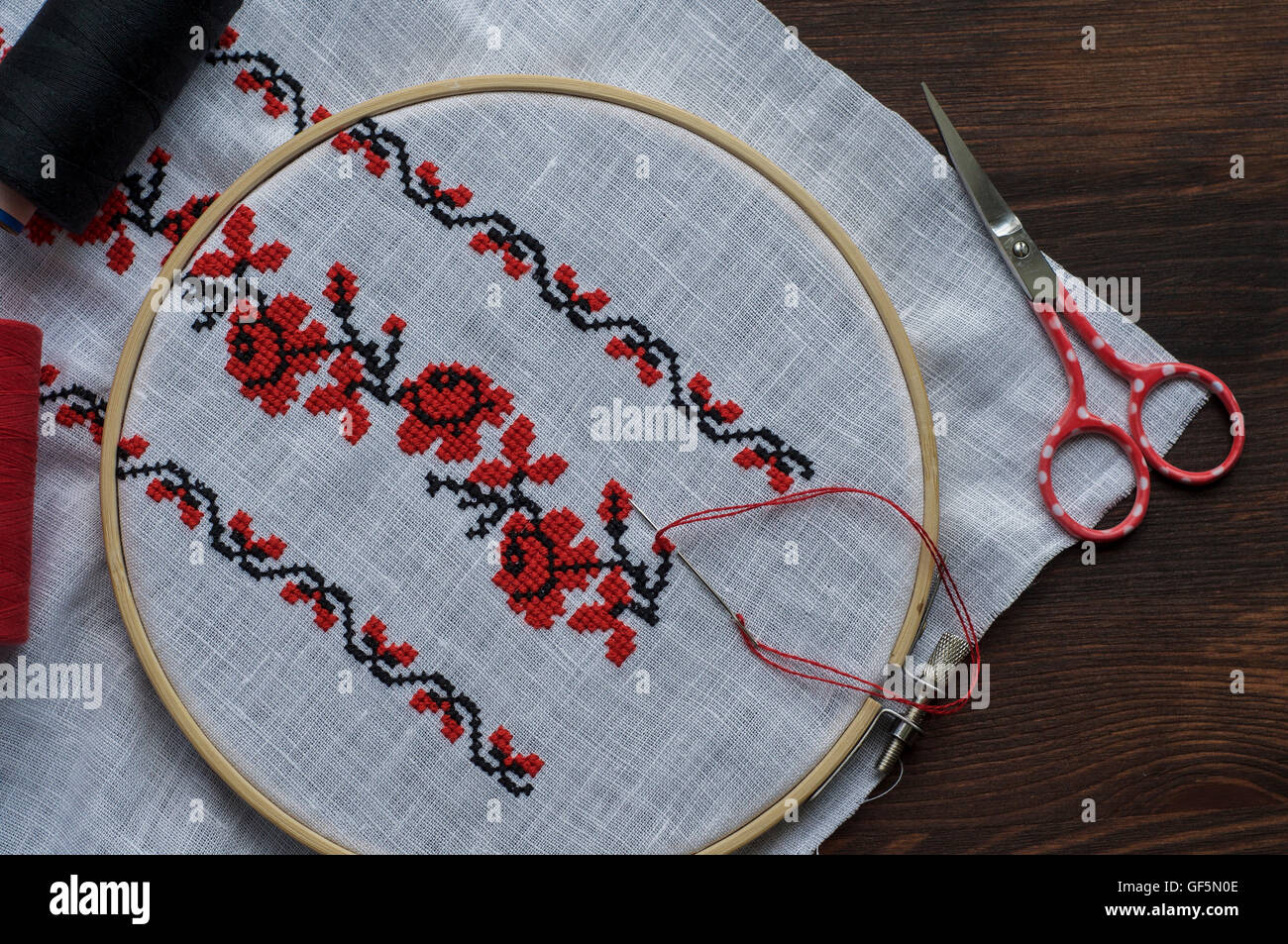 Hand embroidery cross-stitch flower ornament on a white fabric in the wooden embroidery hoop, top view Stock Photo