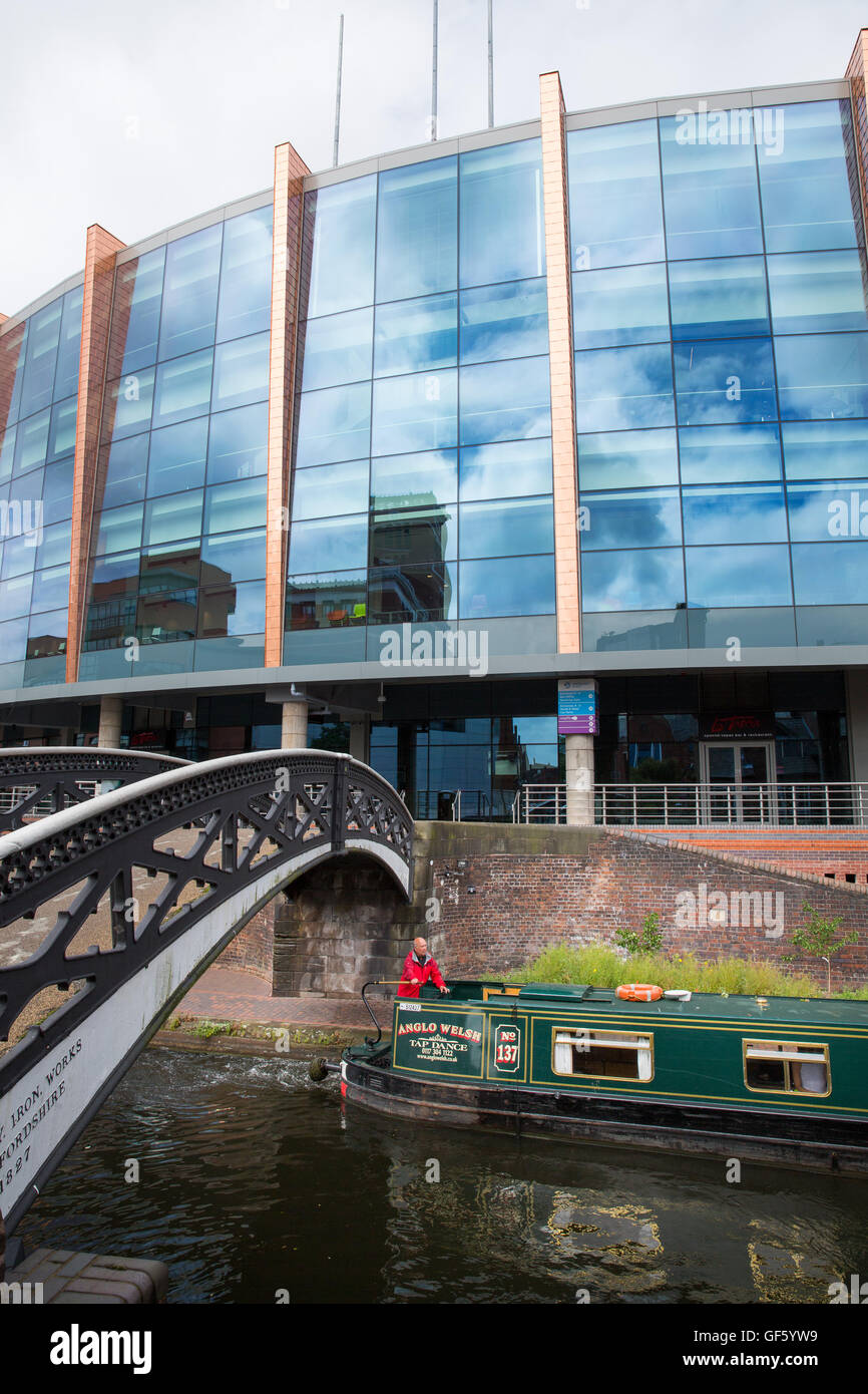 A narrowboat going along the canal in Brindleyplace in front of the National Indoor Arena (NIA). Stock Photo