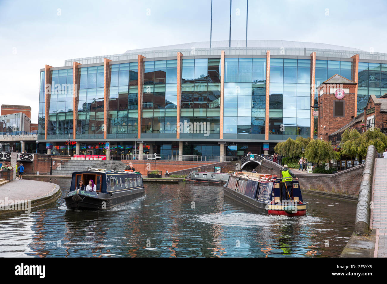 Narrowboats going along the canal in Brindleyplace in front of the National Indoor Arena (NIA). Stock Photo