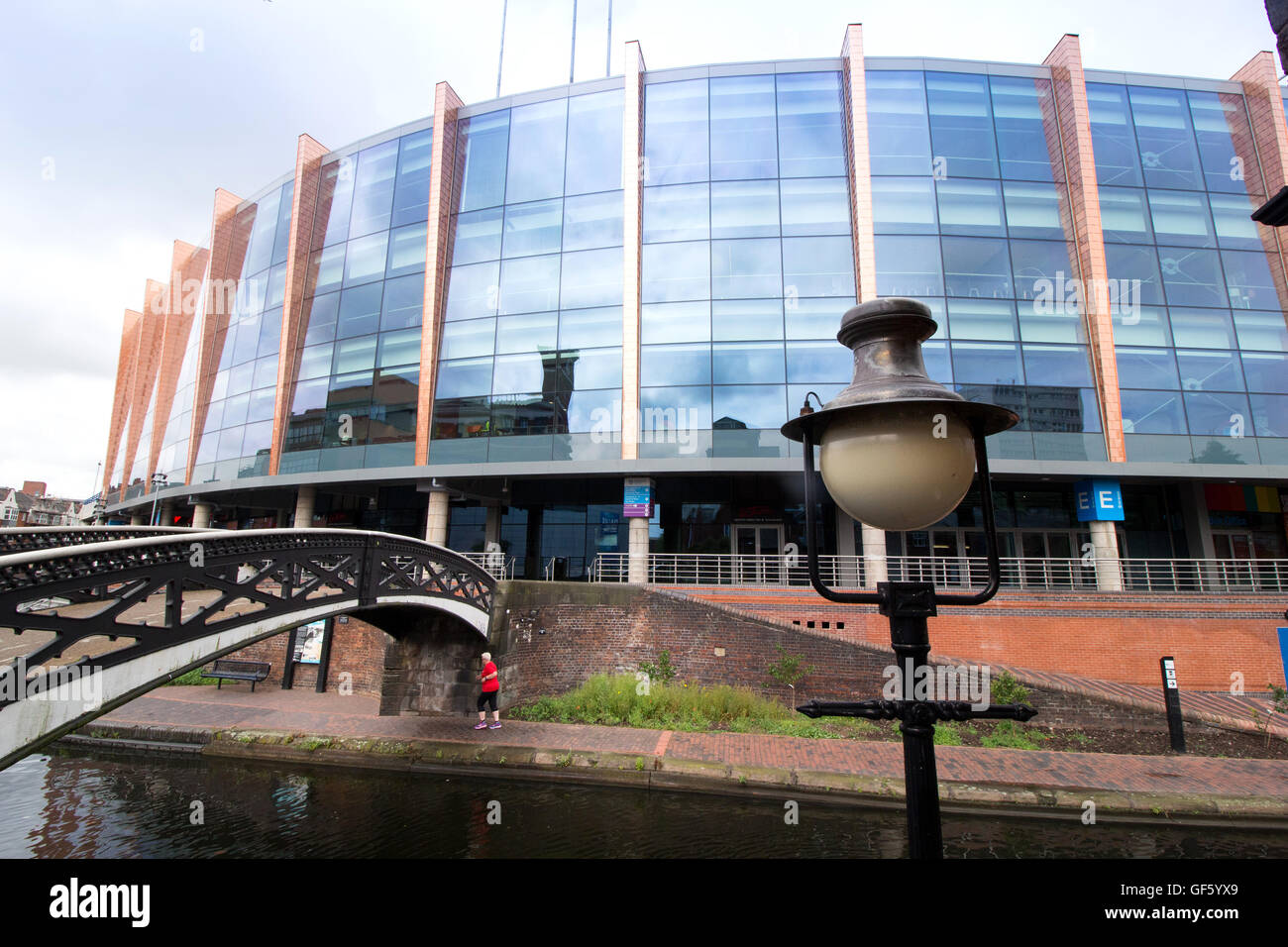 A jogger going along the canal in Brindleyplace in front of the National Indoor Arena (NIA). Stock Photo