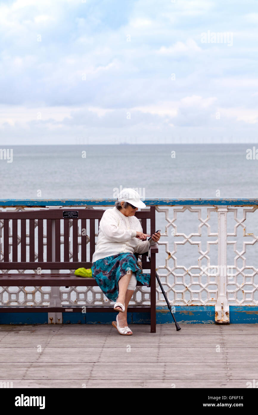 Elderly woman interacting with her mobile device on Llandudno Pier, Wales, UK Stock Photo