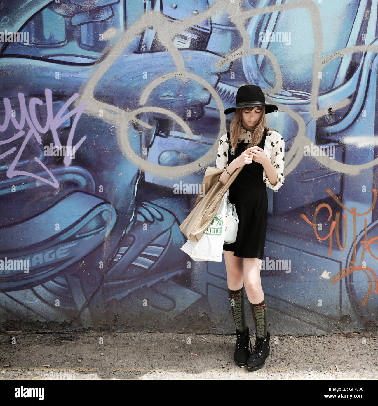 Teenage girl wearing a hat  in front of a mural holding shopping bags waiting for someone Stock Photo