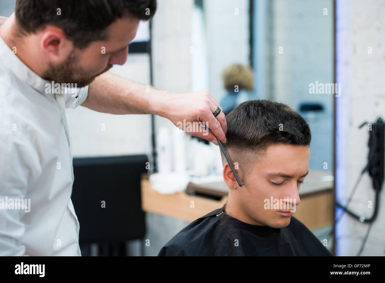 Portrait of handsome man with black hair having haircut at salon. Hairdresser holding comb and scissors. Stock Photo