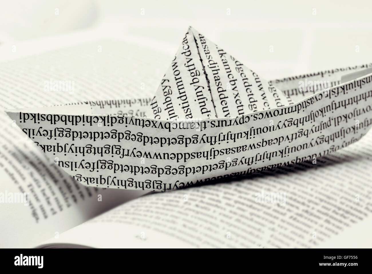 closeup of a paper boat, made with a printed paper with non-sense words, on an open book Stock Photo